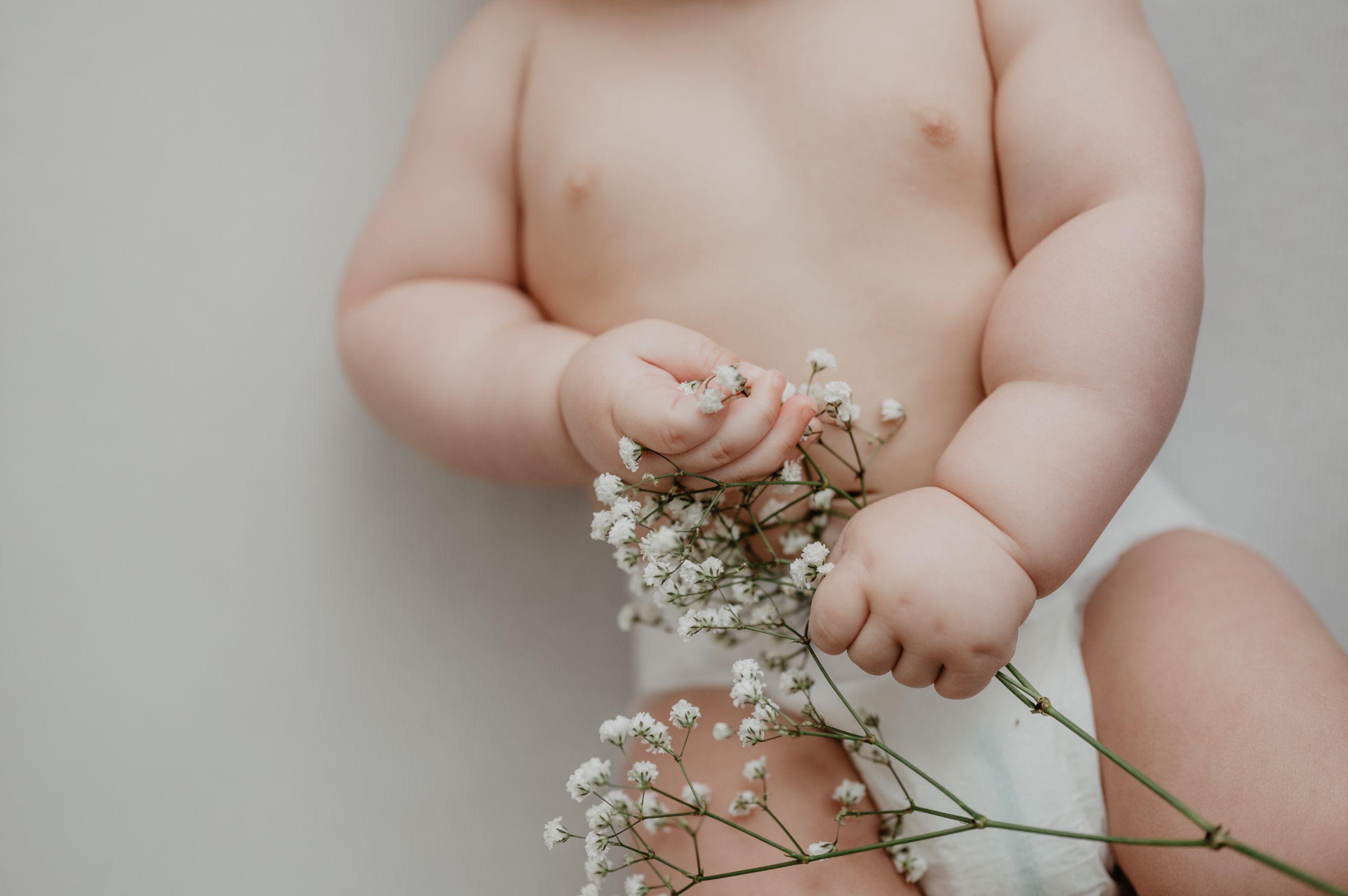 A cute baby gently holding delicate white flowers, symbolizing innocence and new life.